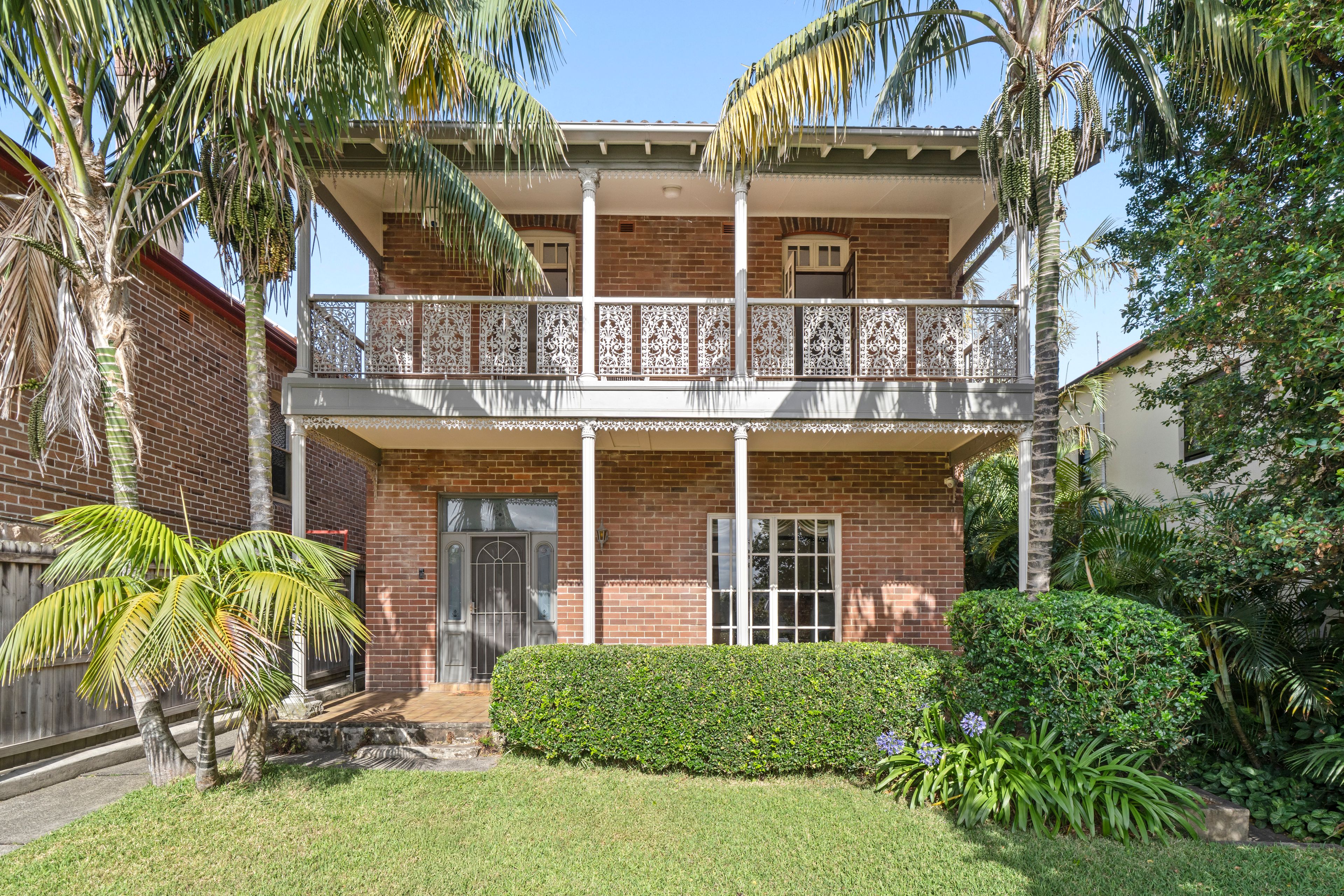 A brick Federation home in Bondi with a white iron-lace verandah, framed by palm trees